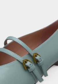 Φωτεινό γαλάζιο δερμάτινο παπούτσι Mary Jane με διπλές λουράκια και αγκράφες σε χρυσό τόνο, με εμφανή ραφή και λεία εσωτερική επένδυση.