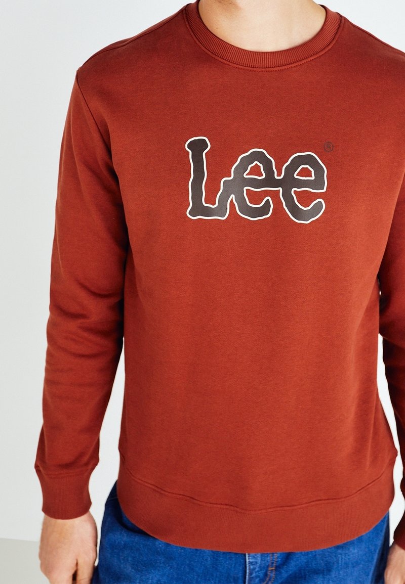 Hnědá bavlněná mikina s kulatým výstřihem, žebrovanými manžetami a lemem. Na přední straně se nachází logo "Lee" obkreslené černou barvou.