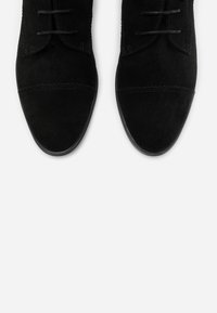 Chaussures en daim noir à finition lisse, dotées d'un bout arrondi, d'un laçage à l'avant et de détails de couture discrets sur le dessus.