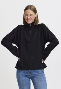 Pullover nero con colletto alto e zip anteriore corta. Caratterizzato da maniche ampie e una vestibilità comoda, realizzato in tessuto morbido e testurizzato.