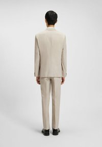 Beige skræddersyet jakkesæt med en slank pasform, der har en notch lapel, enkel slids og matchende bukser. Glat tekstur, klassisk design og mørke sko.