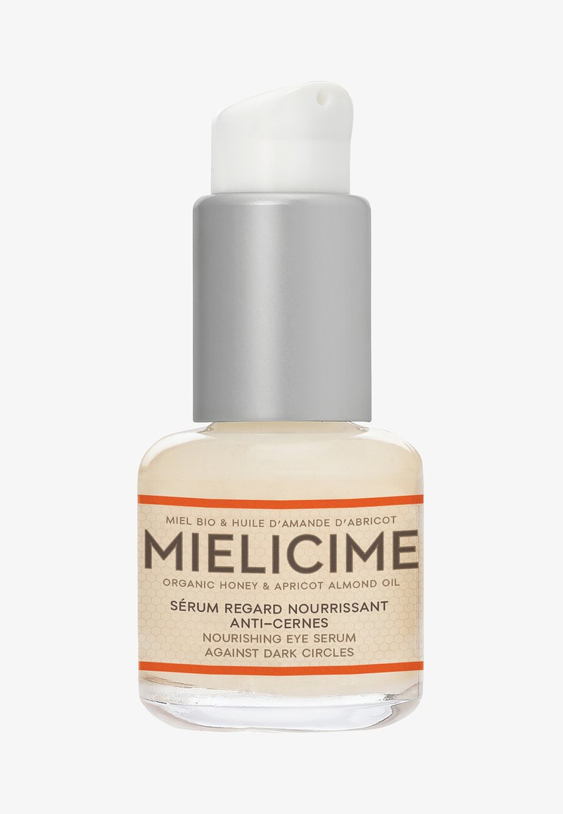 Sérum pour les yeux nourrissant dans un flacon en verre transparent avec une pompe argentée. L'étiquette présente des accents orange et du texte en français et en anglais.