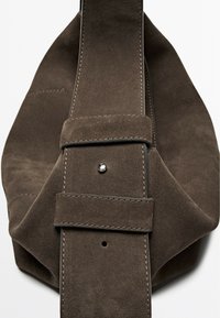 Brown suede bag with a soft texture. Features a wide strap with a metal snap and stitching details. Distinctive draped design.