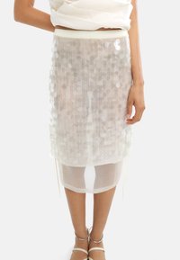 Biała spódnica z cekinami, z pionowymi paskami, warstwowym krojem i prześwitującym dołem. Posiada elastyczny pas i sznurek na końcu.