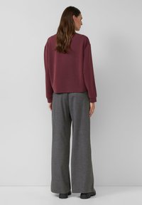 Bordeaux sweatshirt met een relaxte pasvorm en verlengde schouders, gecombineerd met grijze, wijde broekspijpen, beide gemaakt van zachte materialen.