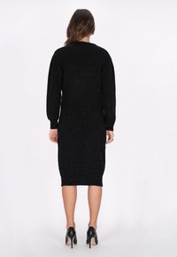 Schwarzes Strickkleid mit figurschmeichelnder Silhouette, langen Ärmeln und gerippten Bündchen. Verziert mit metallischen Einsprengseln, knielangem Saum und Rundhalsausschnitt.