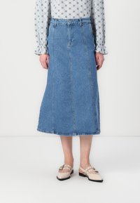 Svetlo modra denim midi krila z vertikalnimi šivi in raztrganim robom. Ujemanje z bež čevlji z naramnicami in dekorativno opremo.