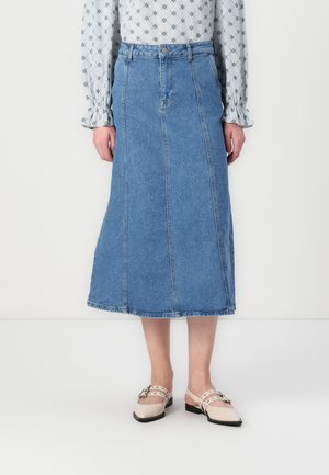 Lys blå denim midi-skjørt med vertikale sømdetaljer og rå kant. Kombinert med beige sko med stropp og dekorativt beslag.