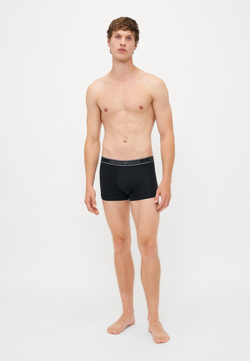 Schwarze Baumwollboxershorts mit einem grauen elastischen Bund, der das Logo "Emporio Armani" trägt. Einfaches Design, formschlüssige Passform, glatte Textur.