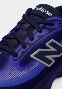 Μωβ αθλητικό παπούτσι με επάνω μέρος από διχτυωτό ύφασμα, εμφανές λογότυπο "N" σε ασημί, υφασμένους σχεδιασμούς και έντονες μπλε ναυτικές λεπτομέρειες. Σχεδιασμένο με κορδόνια και επένδυση στον περιμετρικό λαιμό.