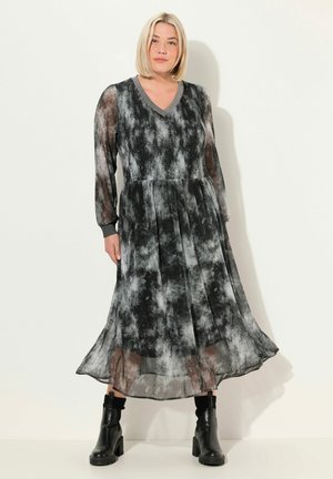 Černobílá šaty s tie-dye vzorem, dlouhými rukávy, výstřihem do V, plisovanou sukní a stažením v pase, doplněné černými kotníkovými botami.