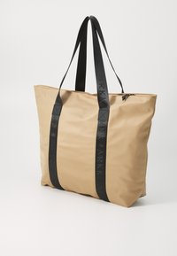Beige nylon bevásárlótáska fekete bőrszíjakkal. Cipzáras záródású, a szíjakon dombornyomott logóval. Kellemes tapintású, tágas kialakítású.