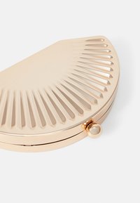 Beige clutch purse with a half-moon shape, featuring ribbed texturing and a gold ball clasp. Made of smooth material with a glossy finish.
