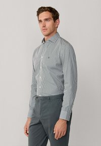 Gestreepte button-up shirt in donkerblauw en wit, met een kraag, een voorflap en een klein logo op de linkerkant van de borst; gecombineerd met grijze broeken.