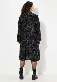 Abito lungo nero con motivo leopardato in grigio, caratterizzato da una vestibilità rilassata e maniche lunghe. Indossato con stivaletti neri alla caviglia.