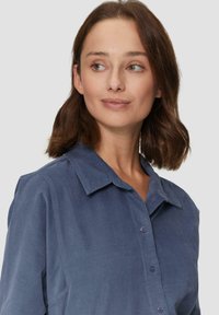 Chemise en velours côtelé bleu marine avec un col pointu, des boutons à l'avant et une finition texturée. Manches courtes et coupe décontractée.