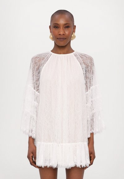 White lace dress with sheer long sleeves, scalloped hem, and floral pattern. Features a round neckline and light, textured fabric.