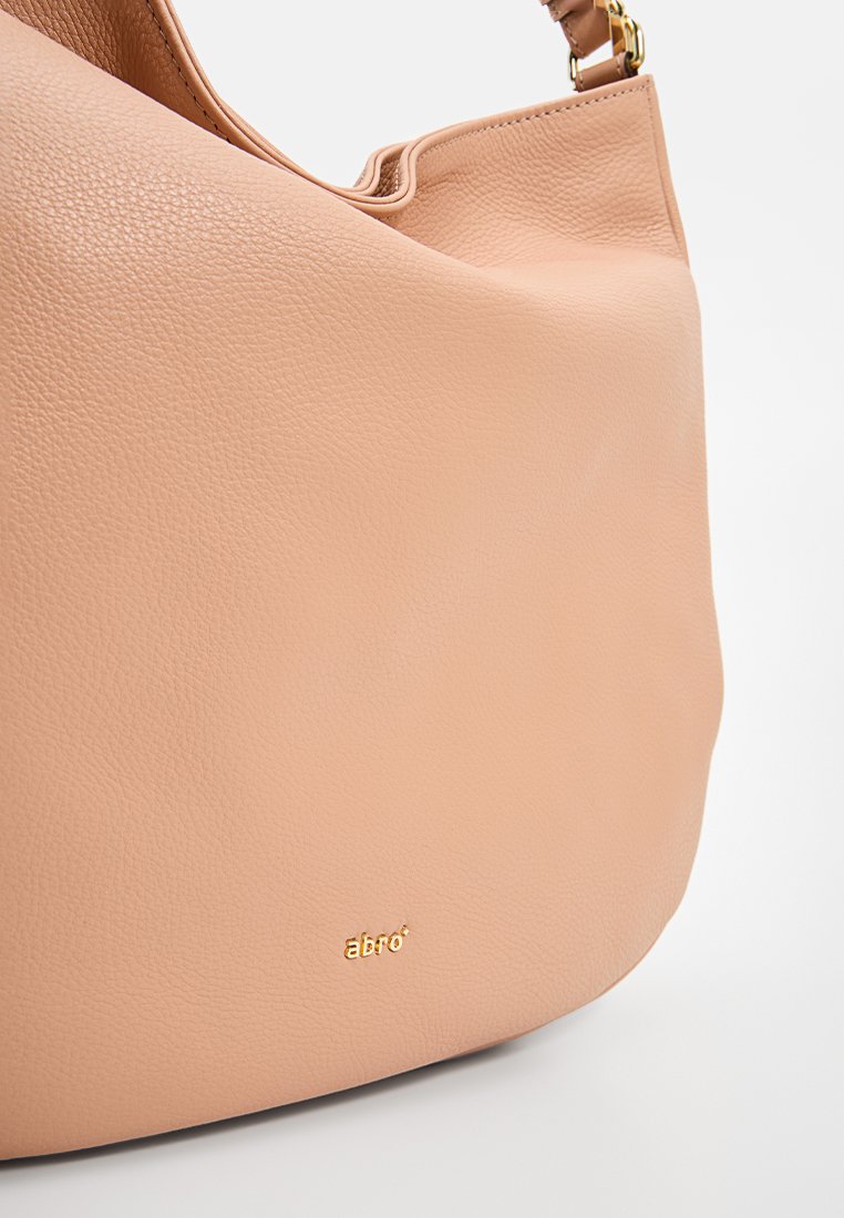 Helle rosa Lederhandtasche mit glatter Textur, geschwungener Form und subtilem goldenen Logo. Verfügt über eine strukturierte Oberseite und einen Schulterriemen.