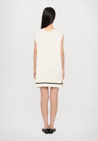 Cream knit dress with short sleeves, featuring a black stripe at the hem. Straight cut and soft texture, back view.