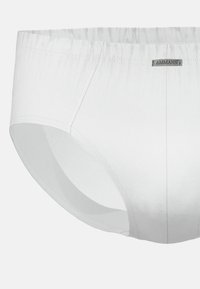 Slip di cotone bianco con lati senza cuciture, elastico in vita e un discreto etichetta con il marchio. Texture liscia con design classico.
