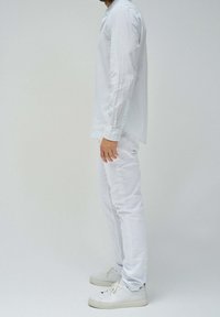 Una camicia a maniche lunghe, a righe light blue e bianche, abbinata a pantaloni bianchi slim-fit e sneakers bianche, con dettagli con bottoni e una vestibilità rilassata.
