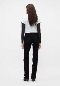 Vaqueros negros desgastados con bordes deshilachados, combinados con una blusa blanca de manga corta y mangas largas transparentes. Diseño simple, ajuste casual.