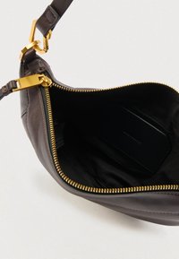 Pruun nahast käekoti sisu, millel on kuldne lukk, tume kangasvooder ja sees ruudukujuline must silt. Üldiselt sile tekstuur.