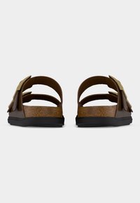 Καφέ δερμάτινα σανδάλια με διπλές λουρίδες και χρυσά αγκράφες, πάτο από φελλό και μαύρη καουτσούκ σόλα, εμφανιζόμενα από πίσω σε λευκό φόντο.
