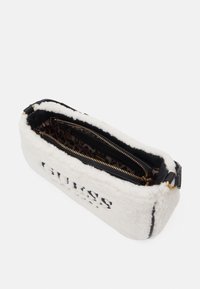 Witte schapenvacht tas met zwarte leren afwerking, voorzien van een ritssluiting en een voering met luipaardprint, met de merknaam aan de voorkant.