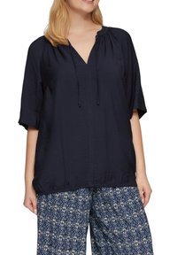 Navyblauw blouse met korte mouwen en een V-hals, voorzien van een trekkoorddetail, met een gestructureerde stof en een geplooide zoom. Gecombineerd met gepatternde wijde broek.