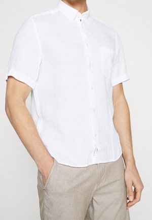 Chemise en lin blanche à manches courtes avec un col boutonné, une poche poitrine unique et une coupe décontractée. Portée avec un pantalon beige clair.