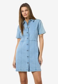 Vestido de camisa em denim azul claro, com mangas curtas, colarinho, fecho frontal por botões e costuras verticais. Textura suave e design ajustado.