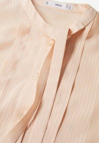 Blouse pêche clair avec rayures verticales, col mao, patte de boutonnage cachée et étiquette indiquant la marque « MNG » ainsi que la taille.