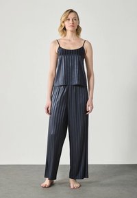 Set di pigiama in satin di colore blu navy scuro con righe verticali. La parte superiore ha spalline sottili; i pantaloni larghi presentano una vita elastica e gamba ampia.