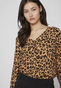 Bluză cu imprimeu leopardo în nuanțe de portocaliu și negru, cu decolteu în V și mâneci lungi, confecționată dintr-un material ușor, cu o textură netedă.