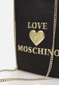 Black faux leather crossbody bag featuring gold metallic lettering "LOVE" and a heart. Includes a gold chain strap with a textured finish.