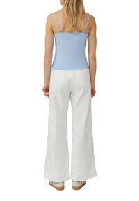 Top in morbido azzurro fitted con spalline sottili abbinato a pantaloni bianchi a gamba larga. Entrambi i capi sono realizzati in tessuto leggero e liscio.