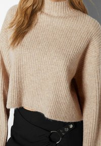 Värjätty neulepusero vaaleanbeigessä pystysuuntaisilla resoreilla. Siinä on korkea kaulus ja pehmeä pinta. Yhdistetty mustaan hameeseen, jossa on metalliset yksityiskohdat.