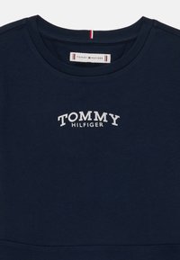 Námornícky modré bavlnené tričko s okrúhlym výstrihom, vyšívaným textom "TOMMY HILFIGER" v bielej farbe a červenými a bielymi akcentmi na golieri.