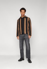 Bruine en zwarte gestreepte jas met een kraag, knoopsluiting en zakken, gecombineerd met donkere jeans en zwarte veterschoenen.