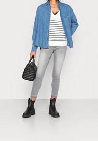 Koszula denimowa, biały top w paski z dekoltem w serek, szare obcisłe dżinsy, czarne botki za kostkę, pikowana czarna torebka. Elementy charakterystyczne to guziki i mankiety na rękawach.