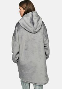 Haut de survêtement gris surdimensionné en tissu doux et pelucheux. Il présente une grande capuche et des manches larges, descendant jusqu'à mi-thigh avec une texture lisse.