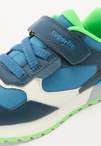 Modrá a zelená sportovní obuv s kombinací syntetických a síťových materiálů, s páskem na suchý zip, texturovanou vnitřní stélkou a vzorovanou podrážkou.