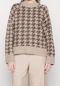 Beige Strickpullover mit einem Hahnentritt-Muster in Dunkelbraun, ausgestattet mit einem gerippten Rundhalsausschnitt und breiten gerippten Bündchen.