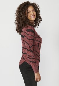 Piros és fekete mintás kötött pulóver hosszú ujjakkal, lekerekített nyakkivágással és enyhe hemline ívvel az oldalakon.