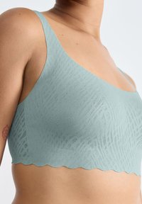 Blød, lys blå bralette med et tekstureret, mønstrede design, bølgede kanter og tynde stropper. Lavet af åndbart materiale.