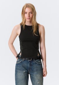 Haut noir sans manches avec des découpes latérales, agrémenté d'accessoires métalliques. Tissu doux avec une coupe ajustée, associé à un jean bleu déchiré.