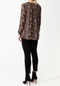 Långärmad blus i ett brunt paisleymönster med svarta detaljer, tillsammans med svarta slim-fit byxor och svarta högklackade ankelstövlar.