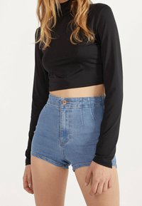 Svart långärmad croppad topp i kombination med högmidjade denimshorts. Shorts har en knappstängning och en ljusblå tvätt med en mjuk textur.