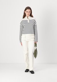 Stripet strikket genser med krage og tre knapper, sammen med hvite jeans med rett ben og svarte loafers. Tilbehøret inkluderer en grønn veske.